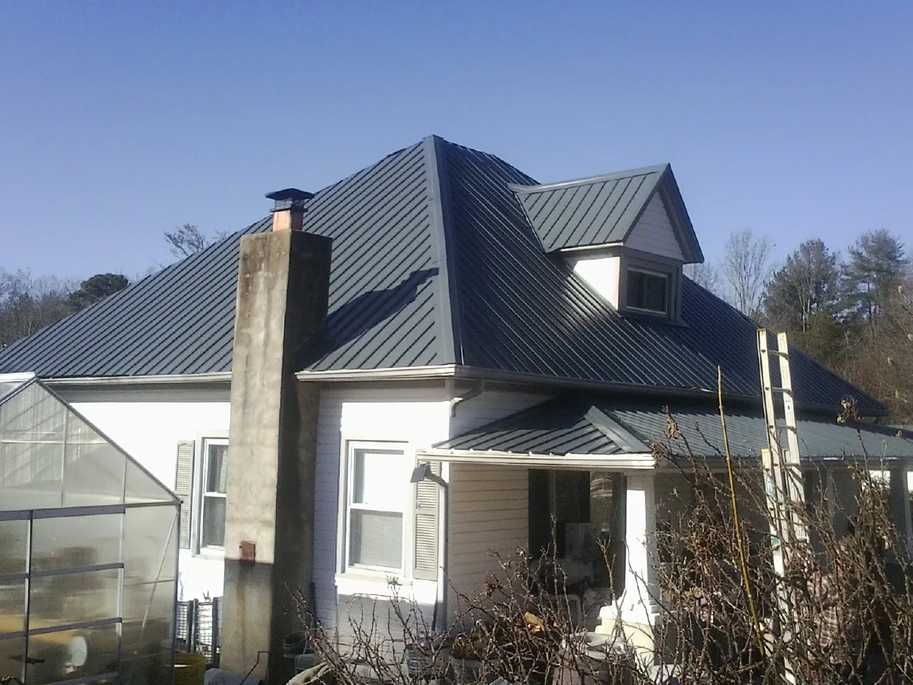 Dark blue standing seam metal roof on a white farmhouse with dormer — Slate & Tile Roof Repair by Roofing Brothers in Honey Creek