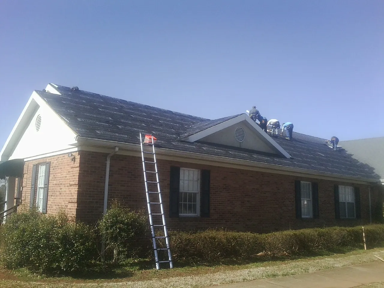 Crew tearing shingles off a brick ranch roof with a ladder set — Metal Roof Repair work by our crew in Honey Creek
