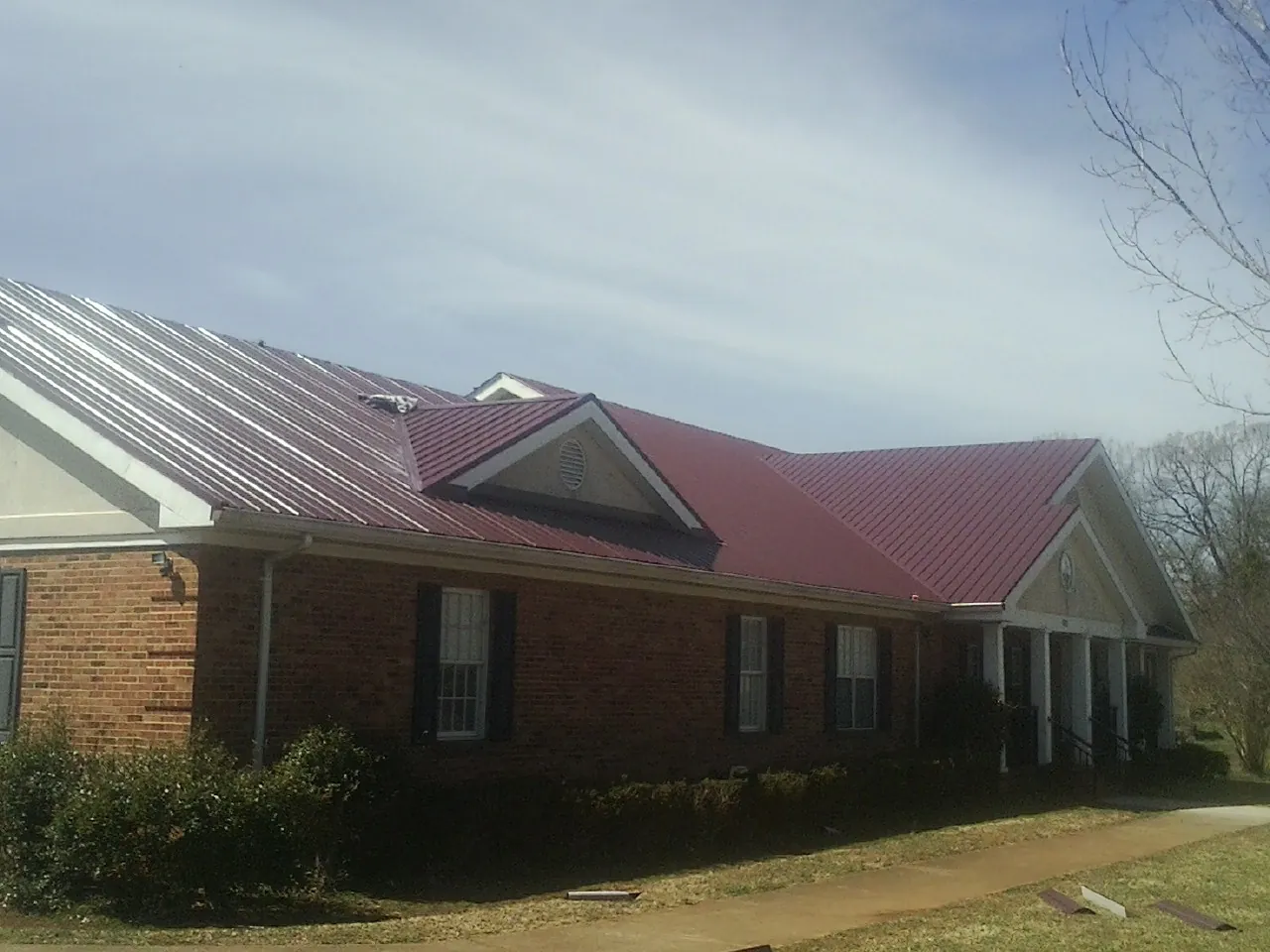 Red metal roof with gabled entries on a long brick building, from a Hail Damage Roof Repair job in Honey Creek