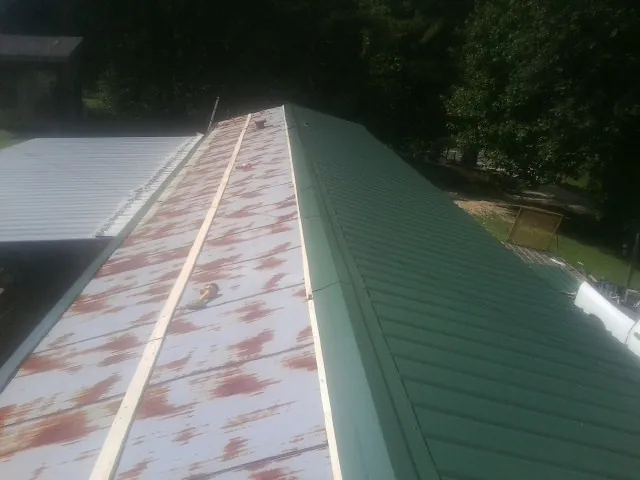 Old rusted panels beside newly installed green metal roofing — Wind Damage Roof Repair by Roofing Brothers in Honey Creek