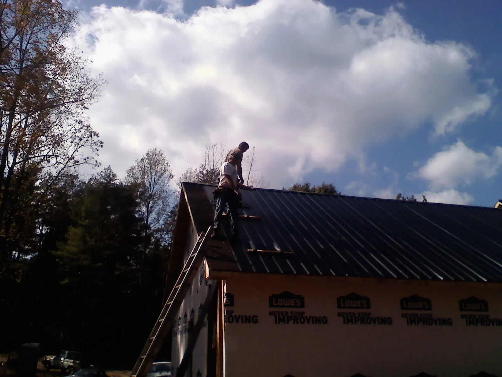 Roofer fastening dark metal panels high against a cloudy sky, from a Roof Inspection job in Honey Creek