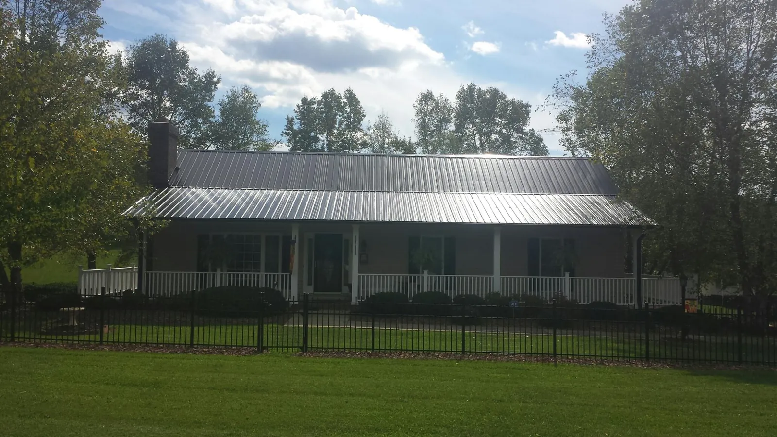 Gray metal roof on a brick ranch with a full width front porch — Gutter Guard Installation work by our crew in Honey Creek