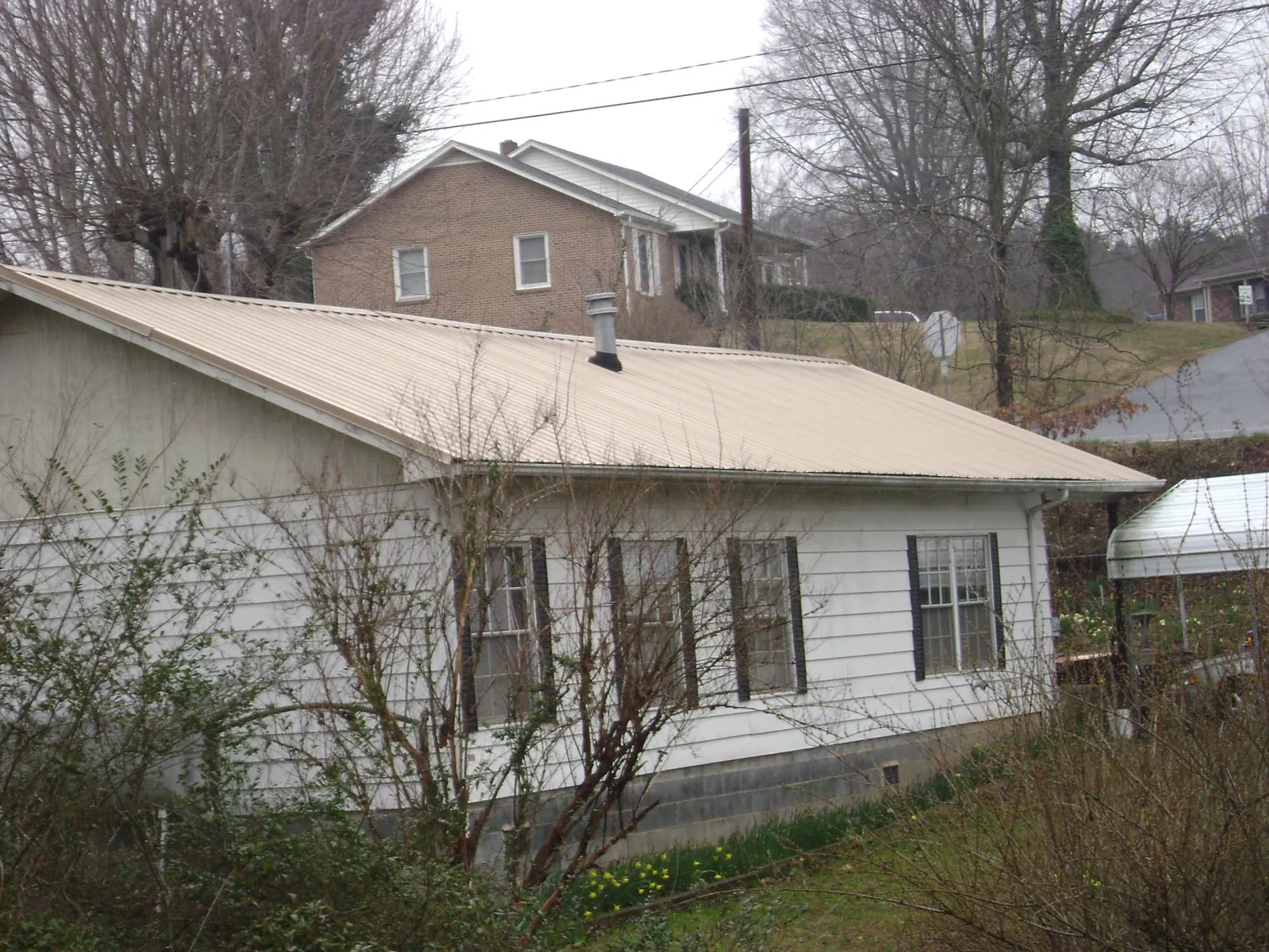 Tan metal roof on a white sided house set into a hillside — Commercial Roofing by Roofing Brothers in Honey Creek