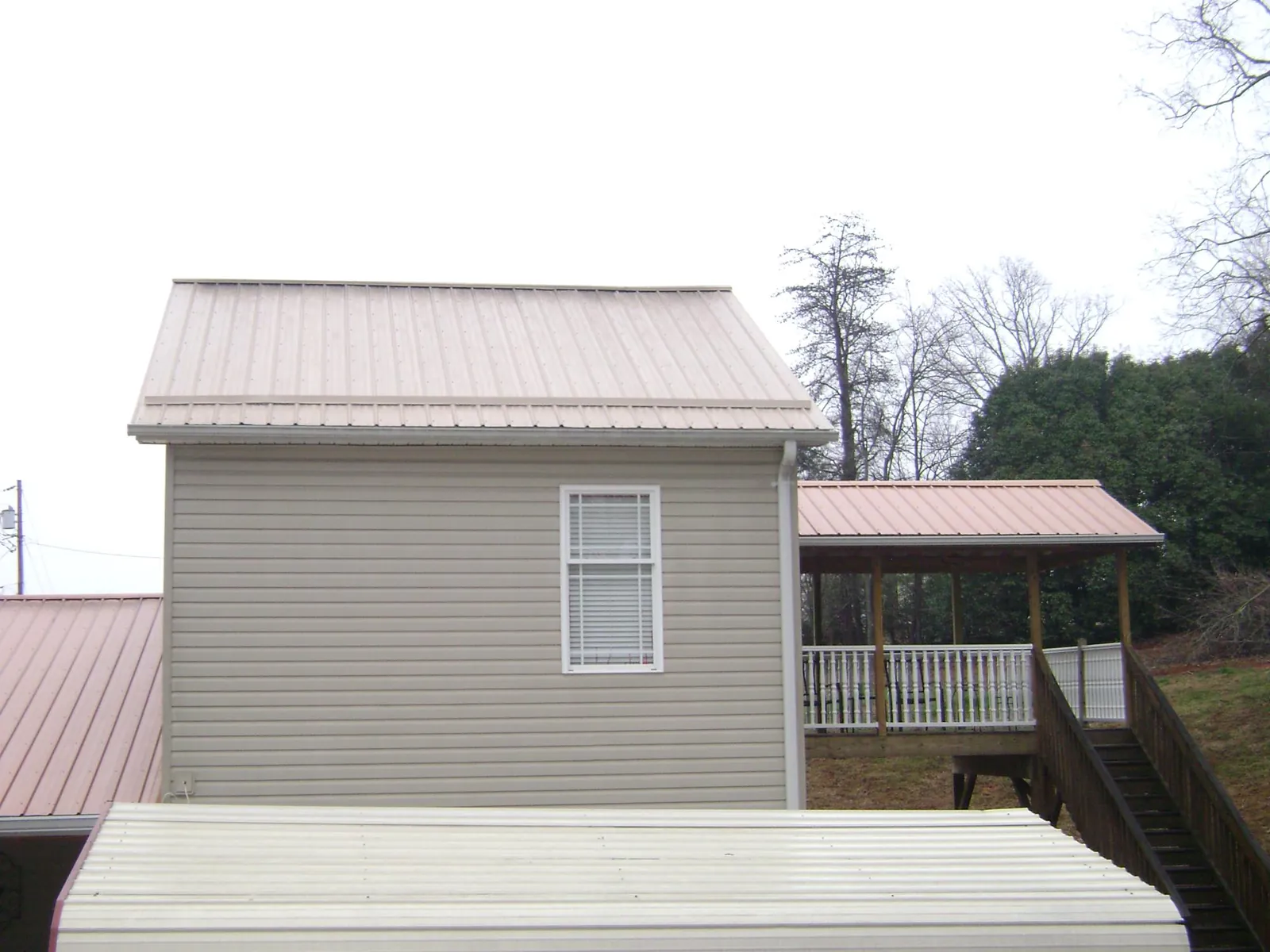Tan metal roofs on a two story addition and attached porch, from a Roof Replacement job in Honey Creek
